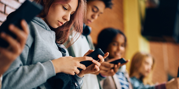 jovens encostados numa parede todos olhando para seus celulares