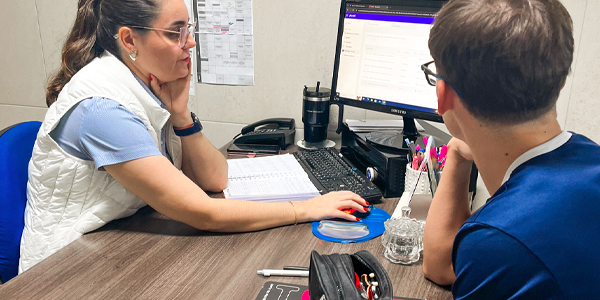 professora e aluno do Colégio Londrinense sentados conversando e conferindo informações no computador